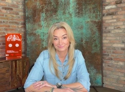 Martyna Wojciechowska, uśmiechnięta i zrelaksowana, przeglądająca swój profil na Instagramie, w tle subtelne nawiązania do jej podróży i działalności społecznej.