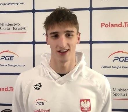 Ksawery Masiuk podczas wyścigu stylem grzbietowym, z widocznym rozpryskiem wody, ukazujący intensywność i siłę sportowca.