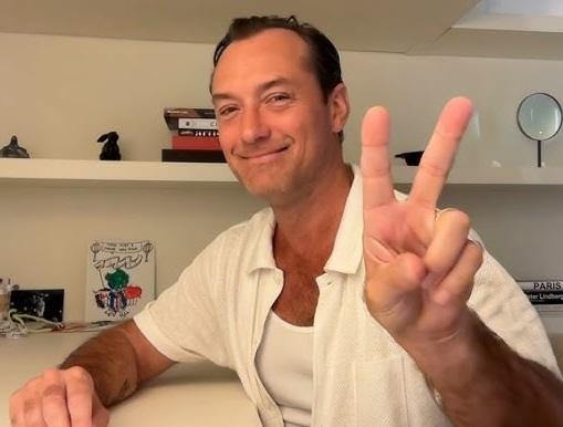 Jude Law w dynamicznej scenie filmowej, ujęty w trakcie akcji na planie zdjęciowym, z filmowym oświetleniem i sugestią ekipy filmowej w tle, podkreślający jego wszechstronność aktorską.