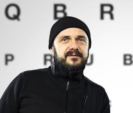 Arkadiusz Jakubik jako wokalista zespołu Dr Misio podczas energetycznego występu na scenie, śpiewający do mikrofonu.
