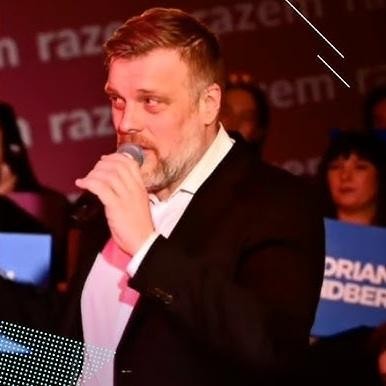Adrian Zandberg podczas dynamicznego wystąpienia publicznego lub debaty, z ekspresyjnymi gestami, ukazujący zaangażowanie w politykę.