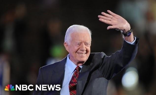 Jimmy Carter podczas budowy Habitat for Humanity, w roboczych ubraniach, uśmiechnięty, w otoczeniu wolontariuszy, symbolizujący jego zaangażowanie humanitarne.