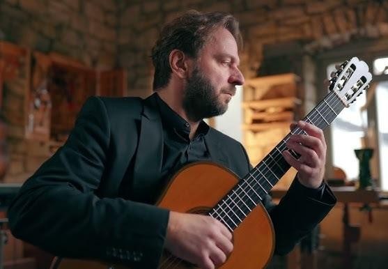 Marcin Dylla w trakcie emocjonującego występu na żywo, grający na gitarze klasycznej.