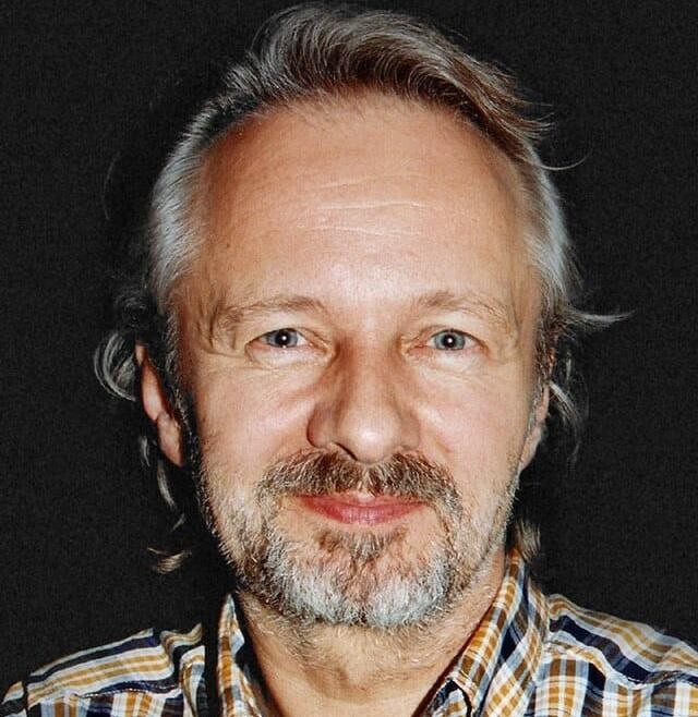 Krzysztof Stroiński w jednej ze swoich ikonicznych ról, uchwycony w dynamicznej scenie filmowej, z wyrazistą mimiką i w charakterystycznym dla jego postaci otoczeniu.