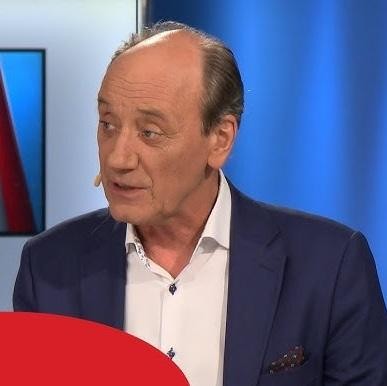 Dariusz Szpakowski w kabinie komentatorskiej, skupiony na relacjonowaniu meczu piłki nożnej, z mikrofonem w dłoni, oddający pasję komentowania na żywo.