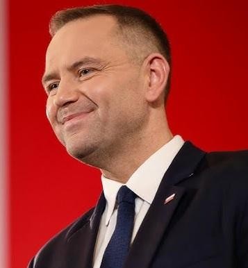 Karol Nawrocki podczas wystąpienia publicznego, z tłem nawiązującym do jego działalności w instytucjach historycznych.