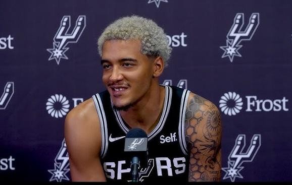 Zbliżenie na charakterystyczną fryzurę Jeremy'ego Sochana i fragment jego koszulki San Antonio Spurs, podkreślające jego unikalny styl i charyzmę.