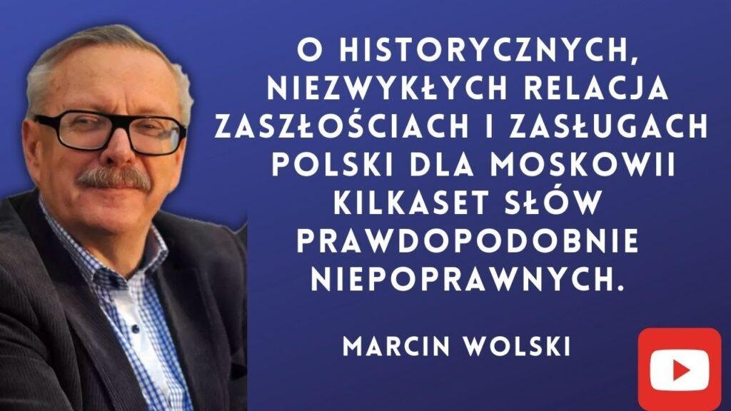 Marcin Wolski podczas pracy, otoczony elementami symbolizującymi jego karierę jako pisarza, dziennikarza i satyryka.