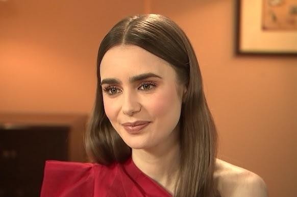 Lily Collins w eleganckiej kreacji na czerwonym dywanie, w tle rozmazane światła wydarzenia.