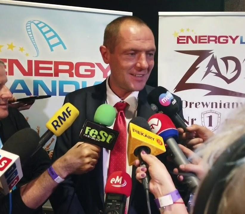 Dynamiczny widok parku rozrywki Energylandia z głównymi atrakcjami i radosnymi ludźmi, symbolizujący sukces Marka Goczała.