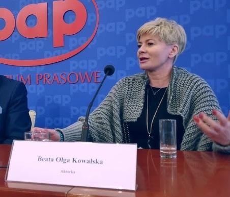 Beata Olga Kowalska na scenie teatralnej, w dynamicznej pozie, oddająca emocje roli, z teatralnym oświetleniem w tle.